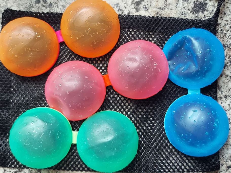 two orange, two pink, two green, and two blue Soppycid Reusable Water Balloons on black mesh bag