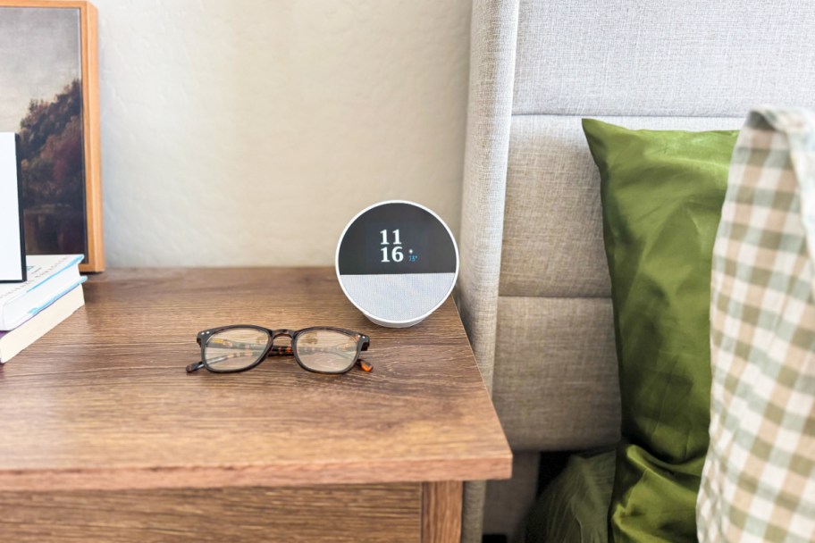 smart alarm clock on nighstand next to glasses and bed frame