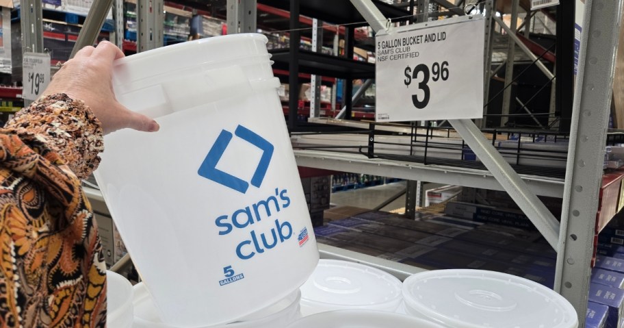 hand holding a white Sam's Club bucket above a stack of more of them, a price sign that says $3.96 is above them