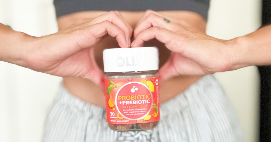 woman making a heart with hands while holding a bottle of OLLY Probiotic + Prebiotic Gummies