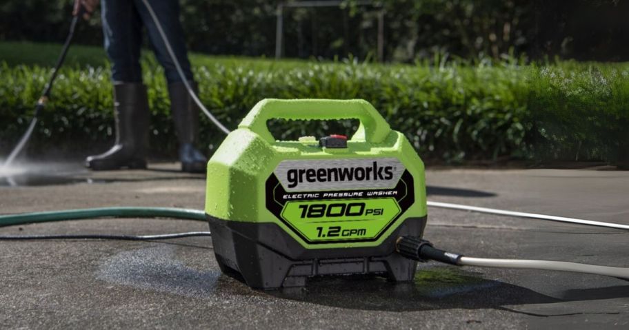 Greenworks 1800 PSI Cold Water Electric Pressure Washer w/ 2 Spray Tips on driveway with person in the background spraying the driveway