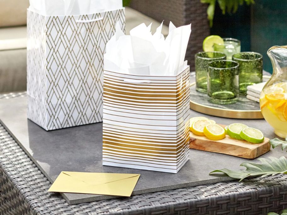 two gold and silver hallmark gift bags sitting on table next to yellow envelope