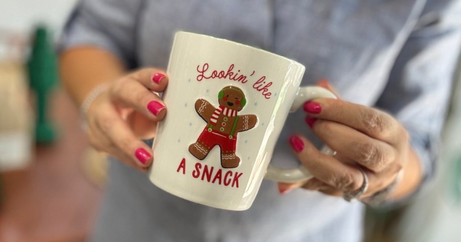 woman's hands holding a Christmas mug in white with a gingerbread man that says "Lookin' like a snack"