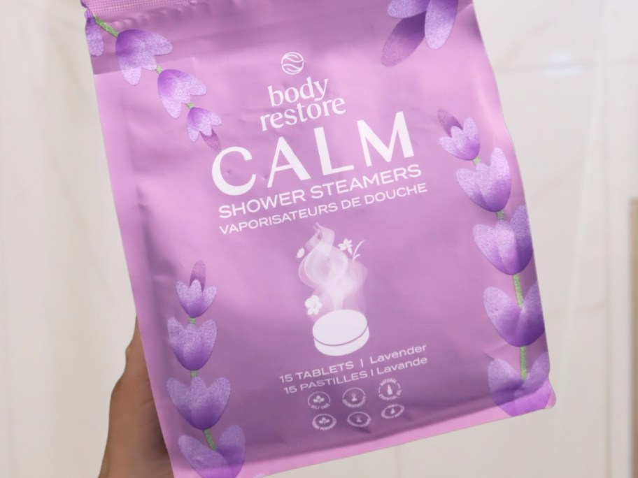 hand holding a purple bag of Body Restore Shower Steamers