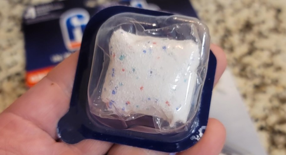 hand holding dishwasher cleaner tablet inside of its packet 