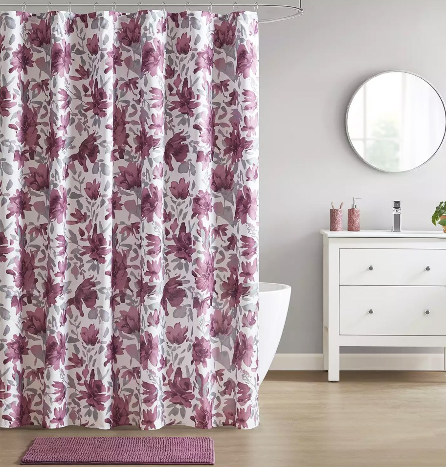 bathroom with a purple floral print shower curtain, coordinating bath rug, and vanity with lotion and soap pumps