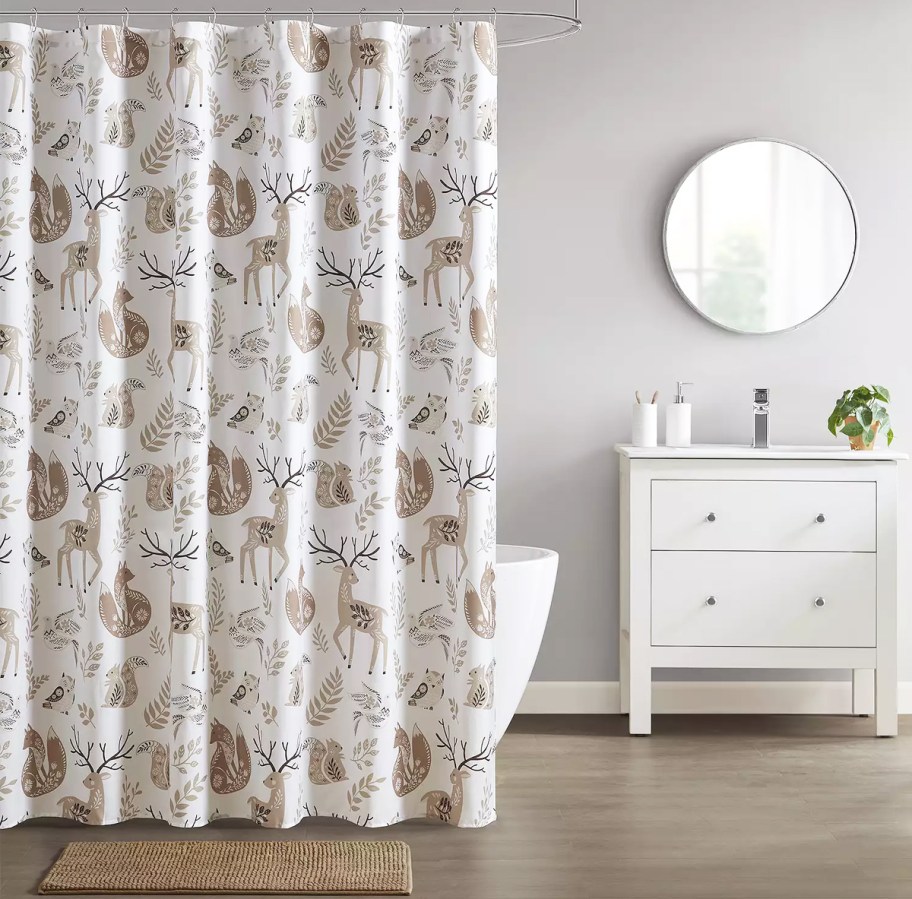 bathroom with a woodland print shower curtain, coordinating bath rug, and vanity with lotion and soap pumps