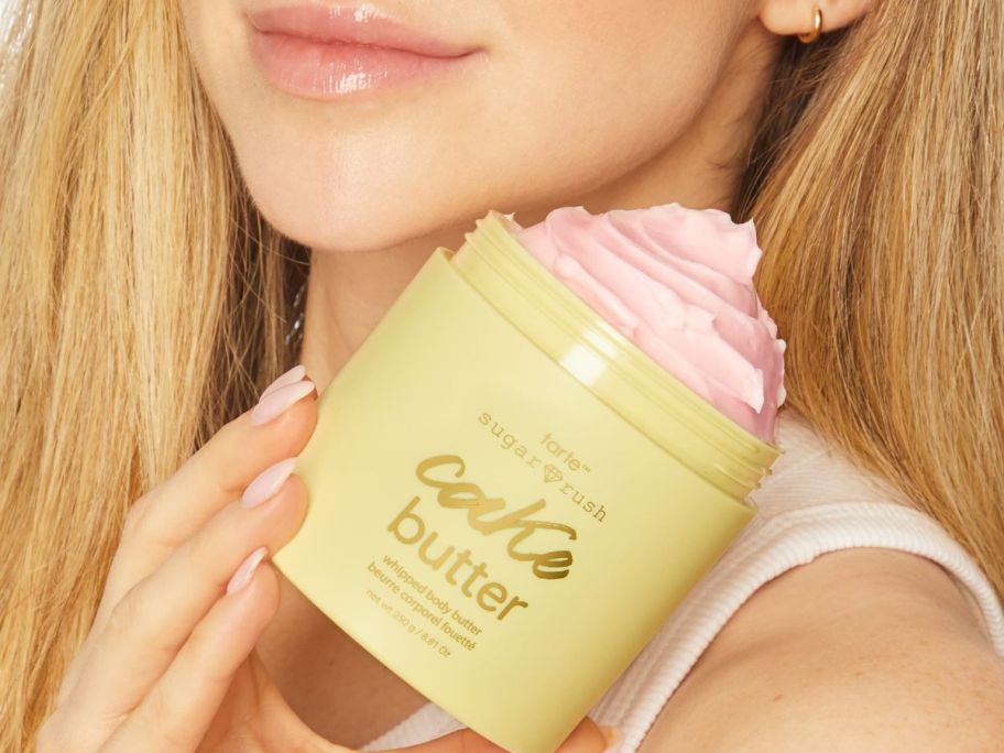 Woman holding a jar of Tarte Cake Butter Whipped Body Butter near her shoulder