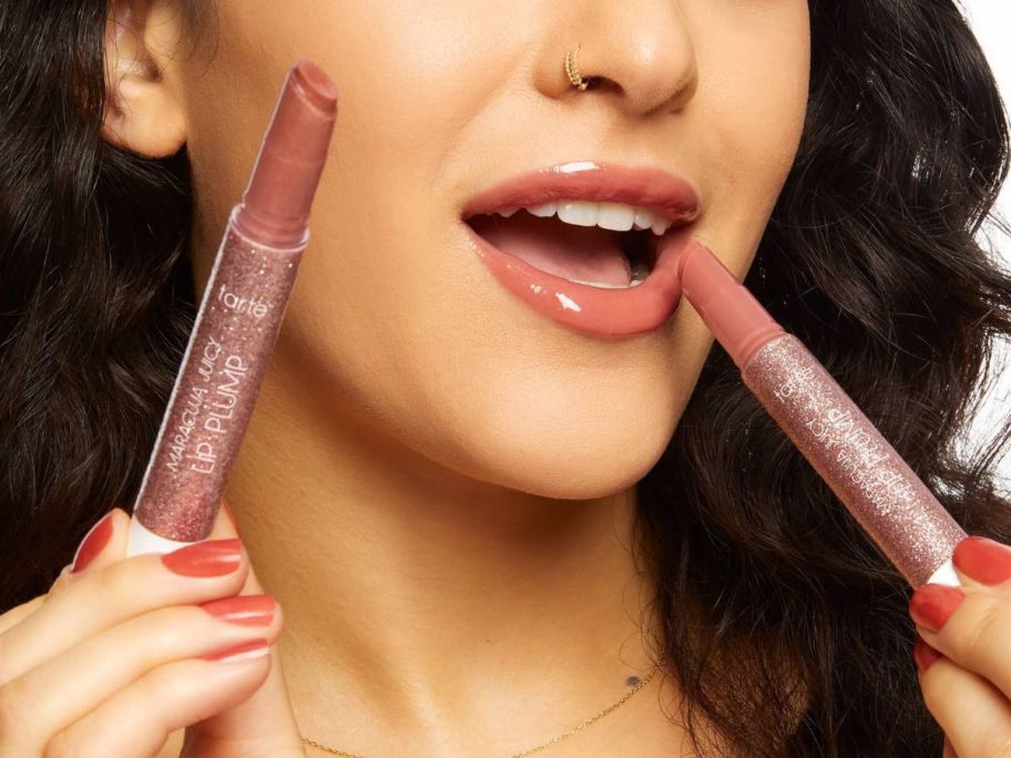 Woman holding two Tarte Maracuja Juicy Lip Plumps