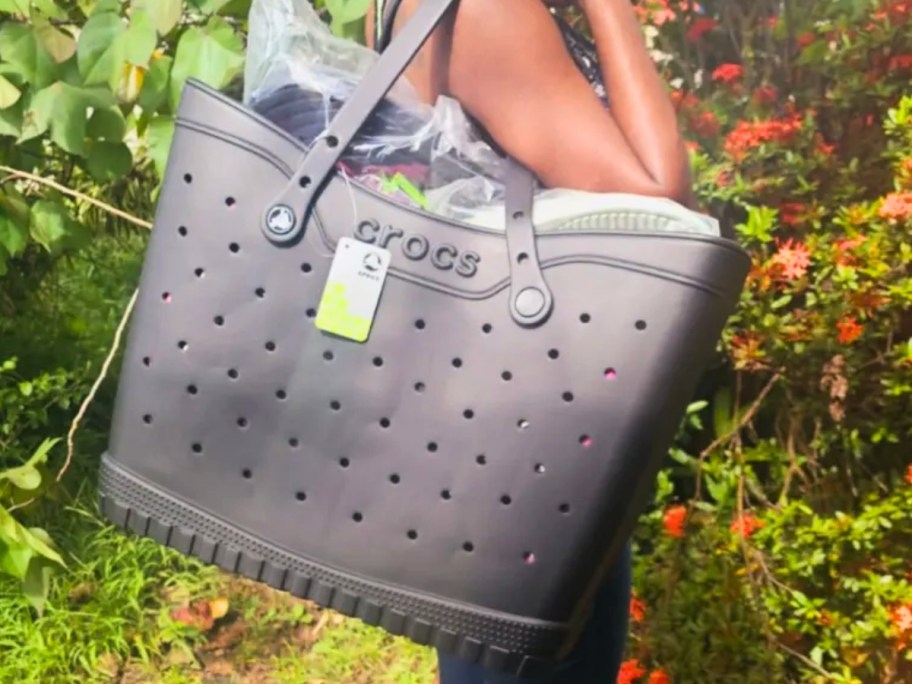 woman standing outside holding a large black Crocs Tote Bag