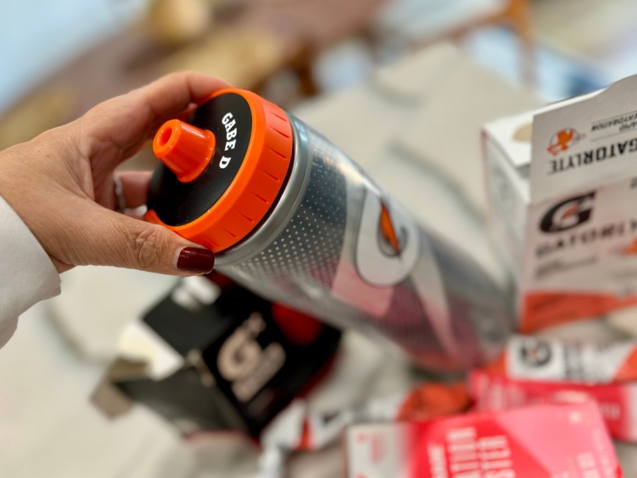 hand holding a silver Gatorade plastic water bottle with a personalized lid and various Gatorade powder and pods packages around it