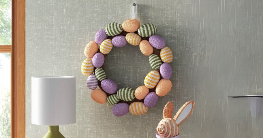 a colorful Easter egg wreath on a wall above a console table with Easter decor on it