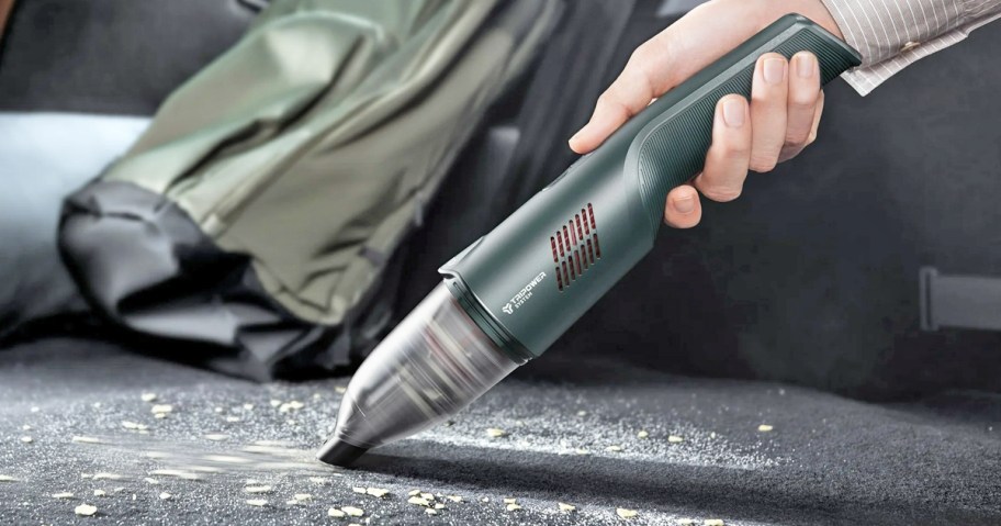using a handheld mini vacuum to clean inside a car