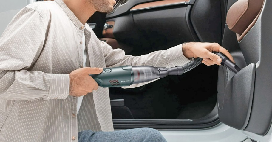 man using a handheld mini vacuum to clean inside car door storage pocket