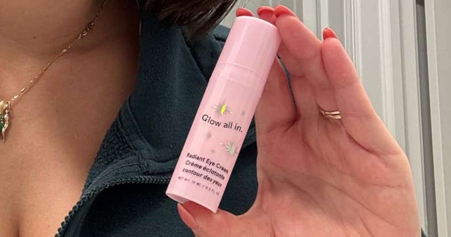 person holding a pink tube of eye cream