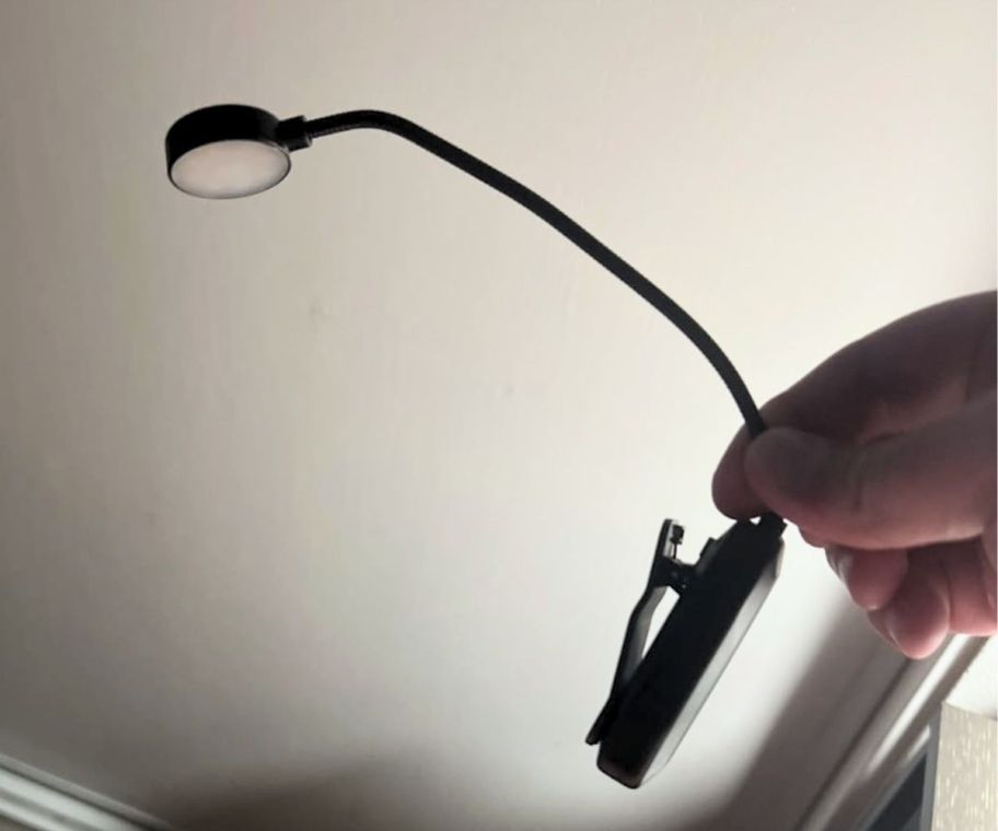 a mans hand holding a round clip on book light