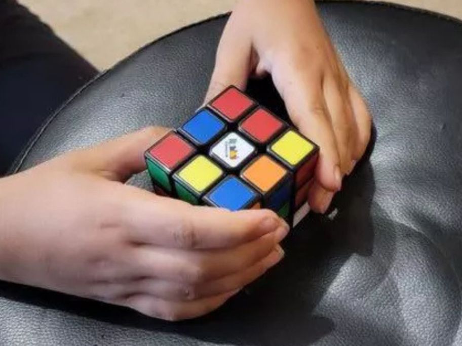 a kid's hands holding a Rubik's Cube Coach Cube on a stool
