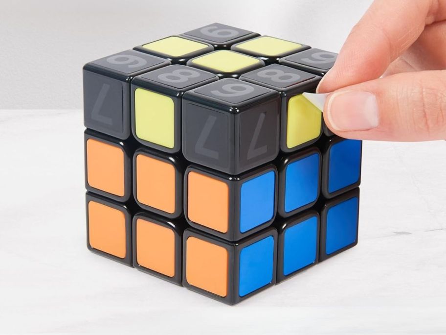 person peeling off a sticker from the Rubik's Cube Coach Cube