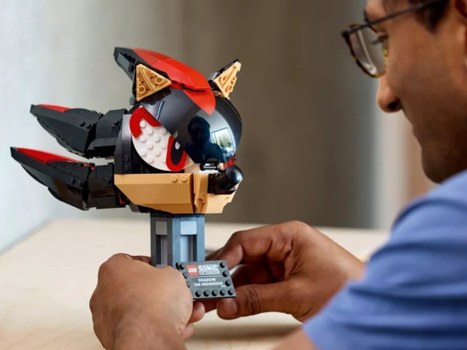 a man putting together a LEGO set shaped like the head of Shadow from Sonic the Hedgehog games and movies