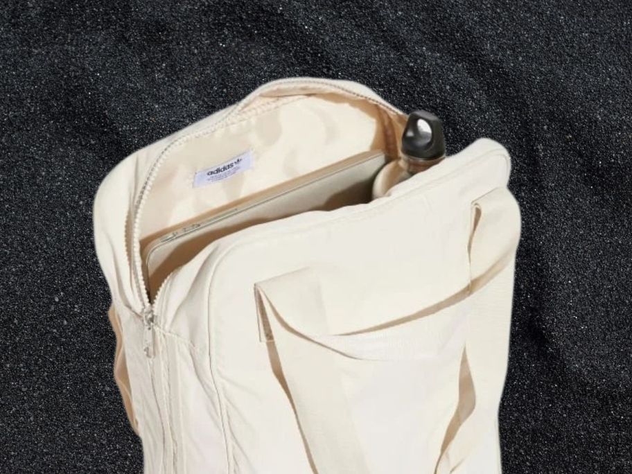 an opened cream colored adidas backpack on a black background