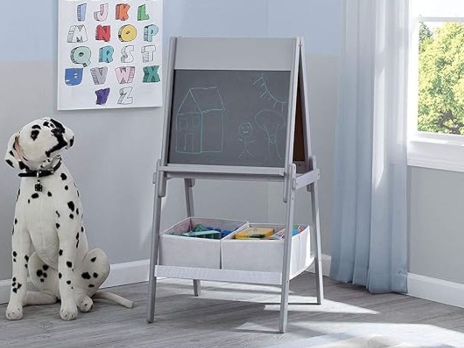 grey Delta Children Activity Easel with black chalkboard side showing with a drawing on it in play room