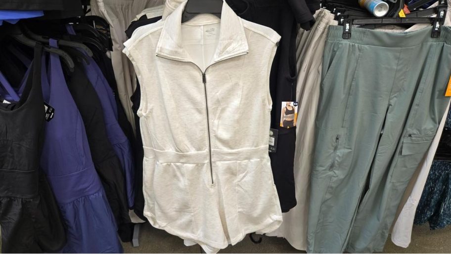 White zip-front sleeveless Avia knit romper hanging on a store rack with similar activewear.