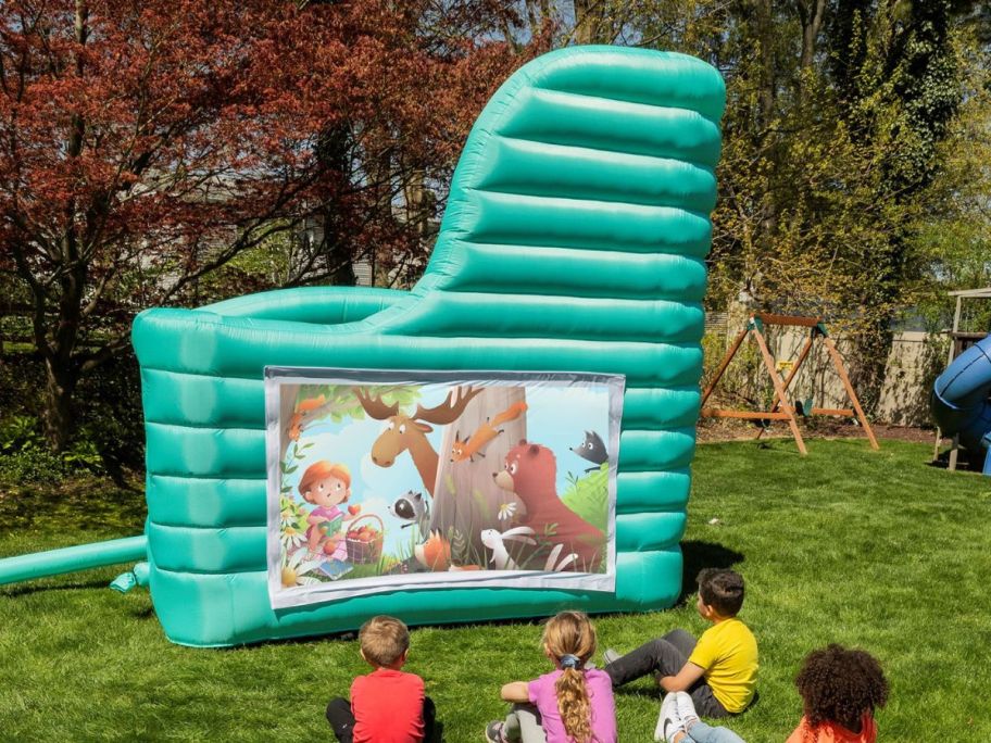 Kids on a lawn watching a projector screen on a bounce house