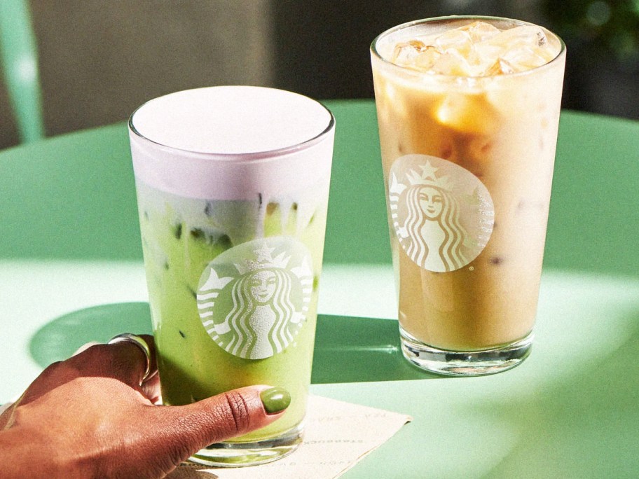hand touching a starbucks glass with green beverage with an iced drink in background
