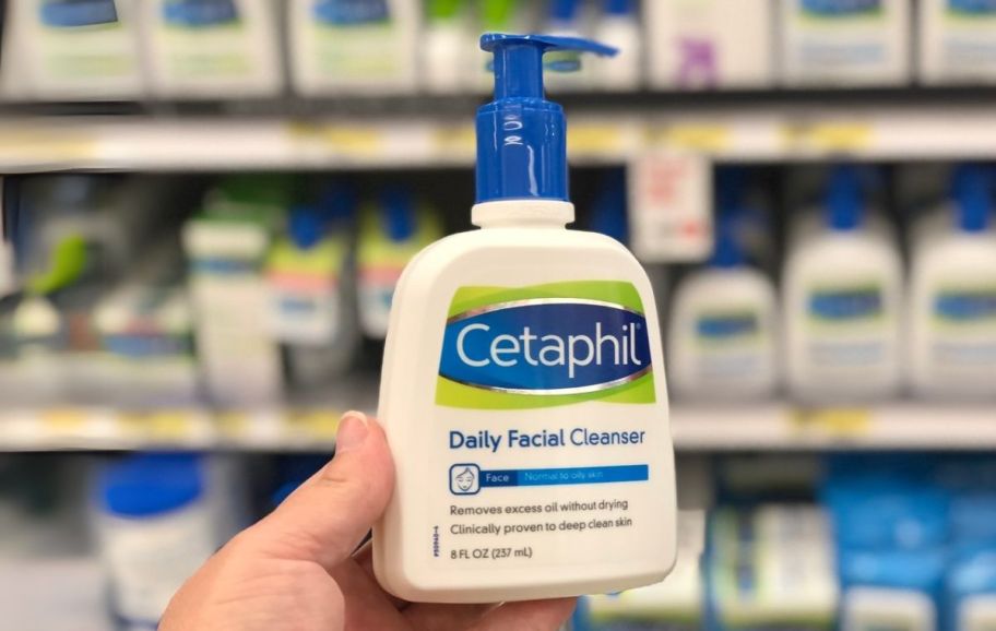 a womans hand holding a bottle of facial cleanser