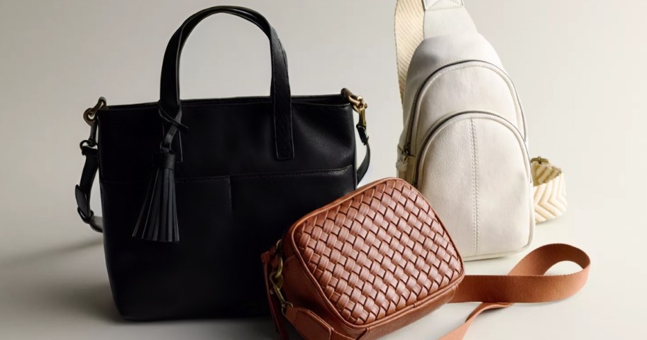 a black tote style purse, a brown woven camera bag style purse, and a cream sling bag style purse