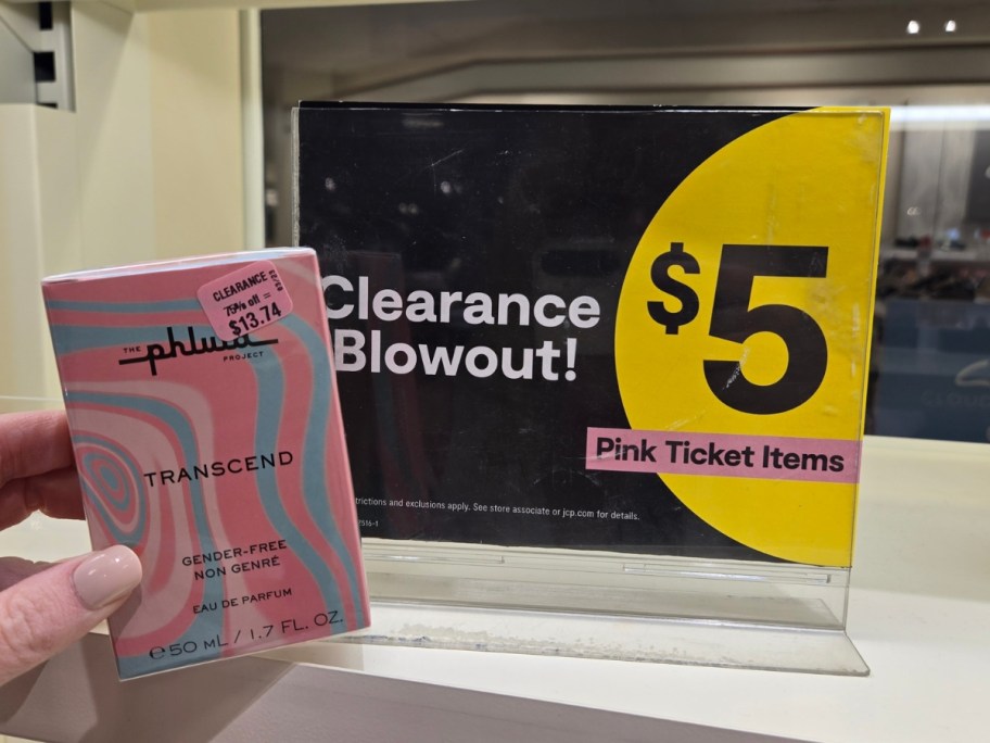 hand holding a box of perfume in front of a clearance sign in a store