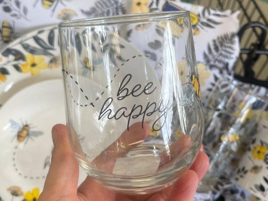 Hand holding up a Bee Happy Dollar Tree Stemless Wine Glass