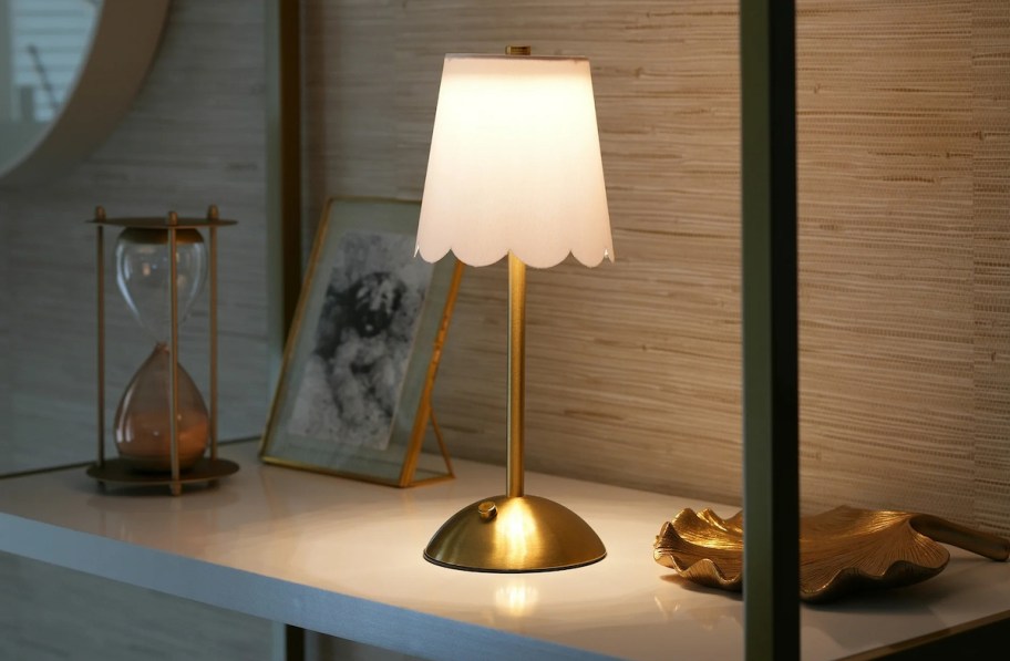 cordless brass and white lamp on bookshelf