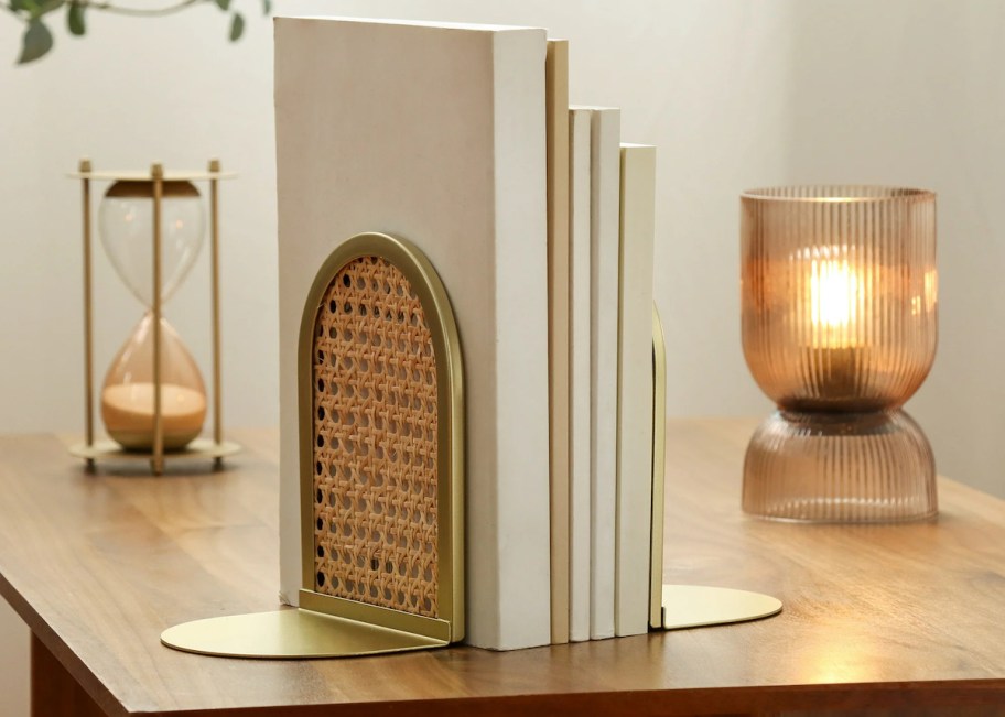 gold and rattan bookend holding stack of neutral books on wood table