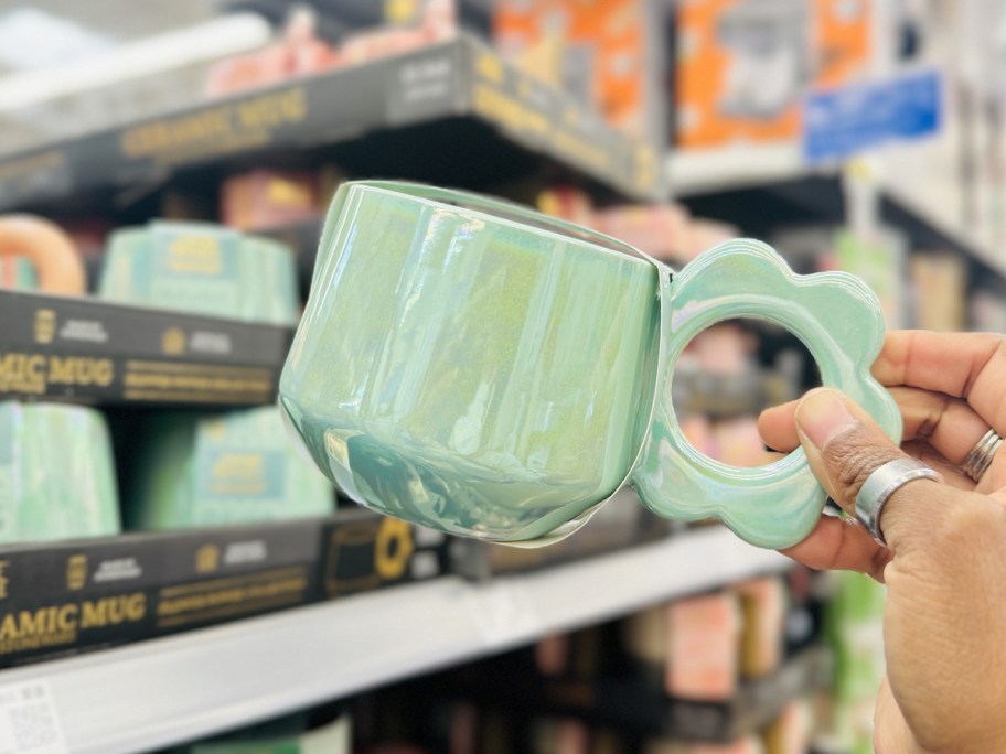 hand holding a green pearlescent coffee mug with a flower shaped handle