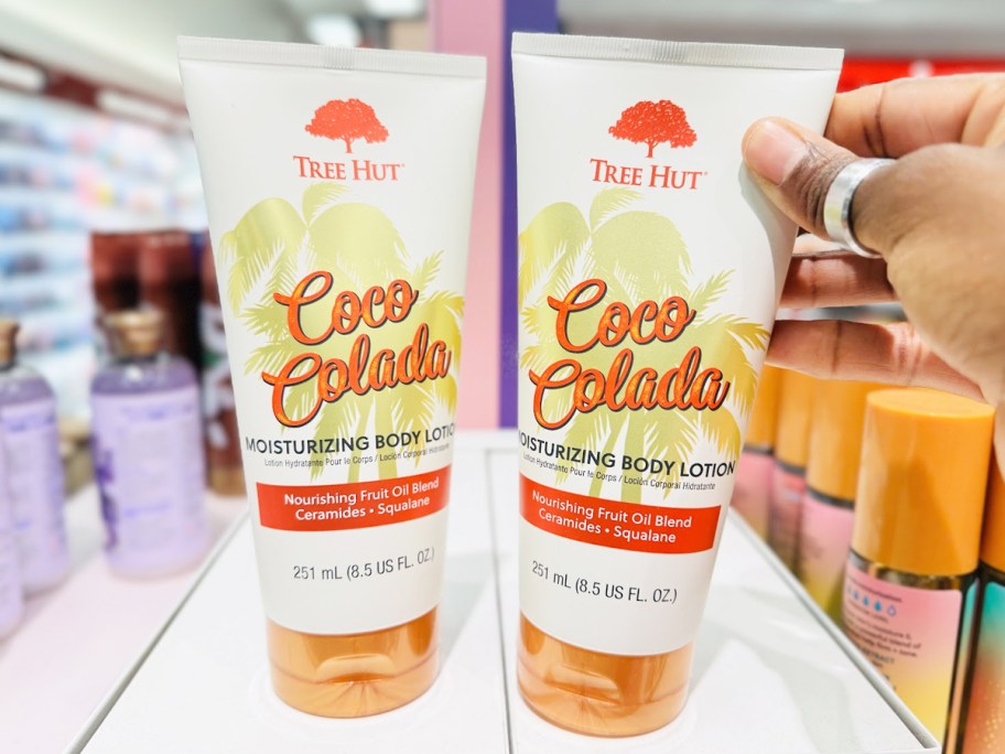 hand touching two white bottles of Tree Hut Moisturizing Body Lotion on store shelf