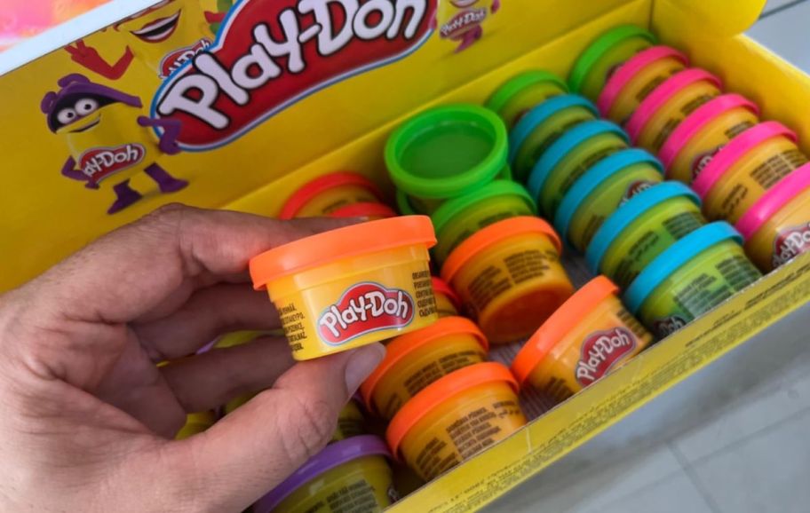 mans hand holding a can of play doy in front of a 42 count box of play doh fun size cans