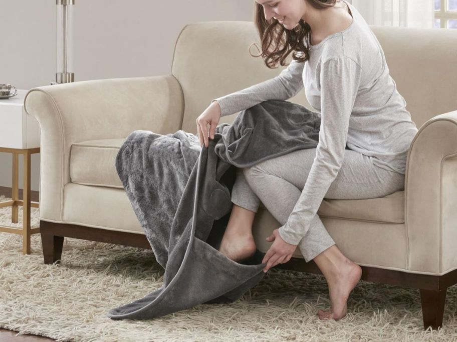 woman sitting on couch and putting foot into pocket of beautyrest Heated Throw Blanket