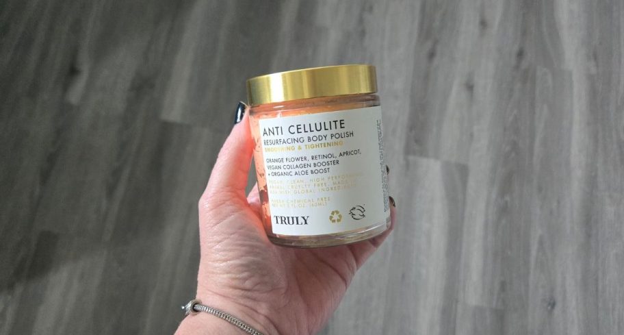 a womans hand holding a jar of body polish