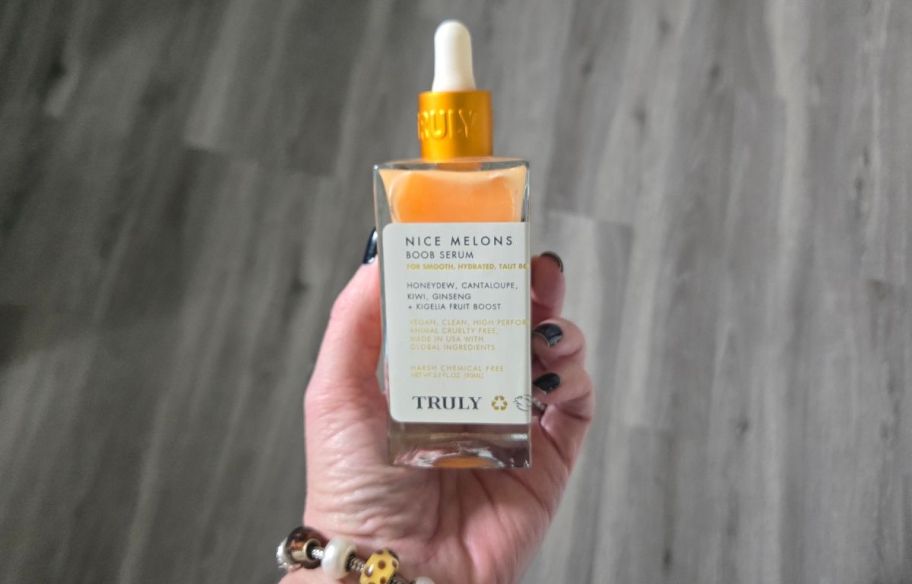 a womans hand holding a bottle of body serum