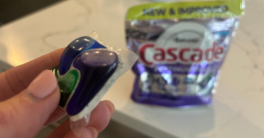 Person holding up singular cascade dishwasher detergent pod in front of nine count bag