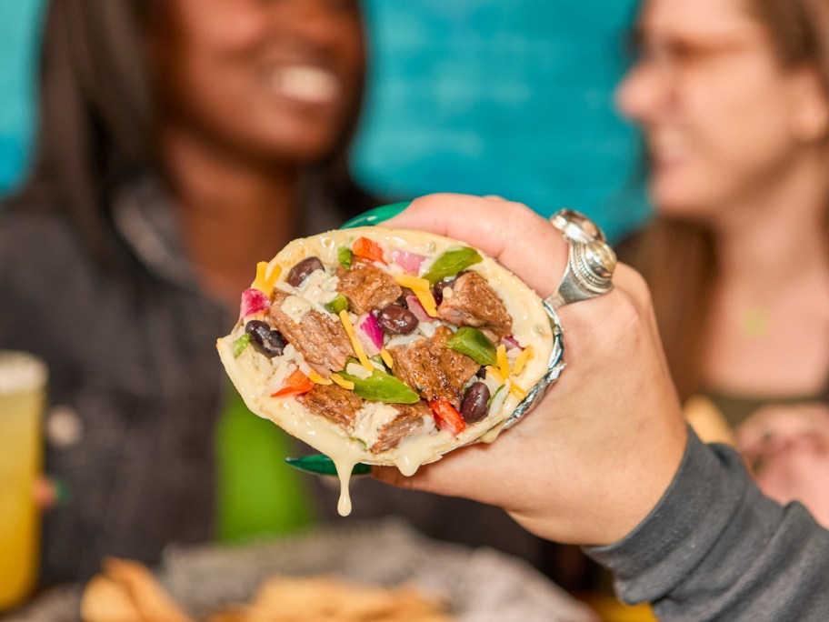 holding a burrito that's dripping with queso
