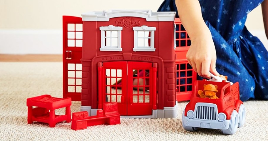 child playing with a red fire station playset on floor