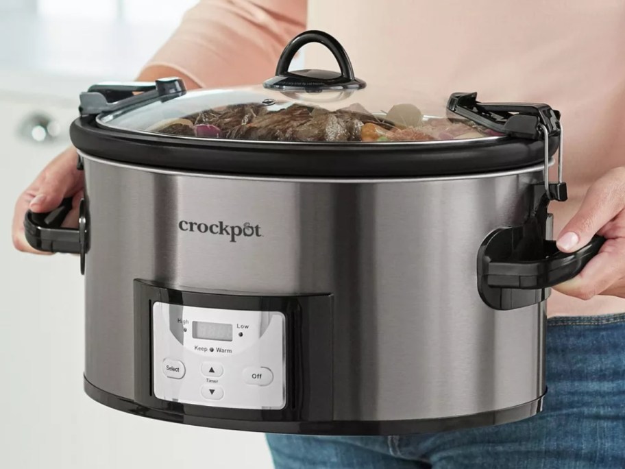 woman holding a large stainless steel CrockPot