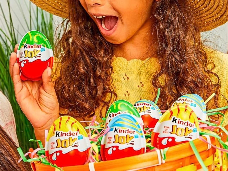 Little girl excitedly holding a Kinder Joy Egg while holding a basket full of them
