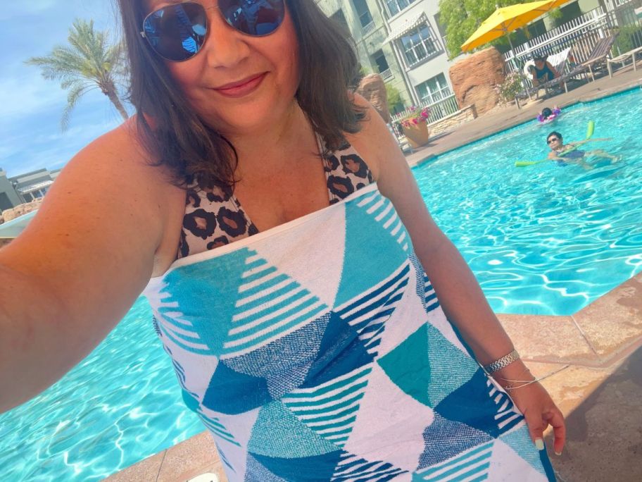 woman wrapped in a The Big One Beach towel while sitting poolside