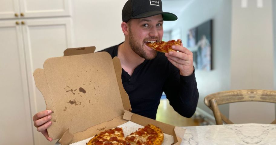 man eating a slice of pepperoni pizza from a box with a whole pizza in it