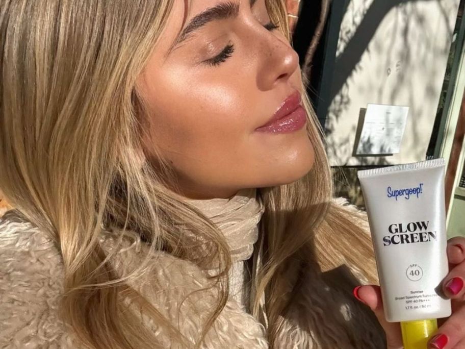Woman holding a Supergoop Glowscreen next to her face