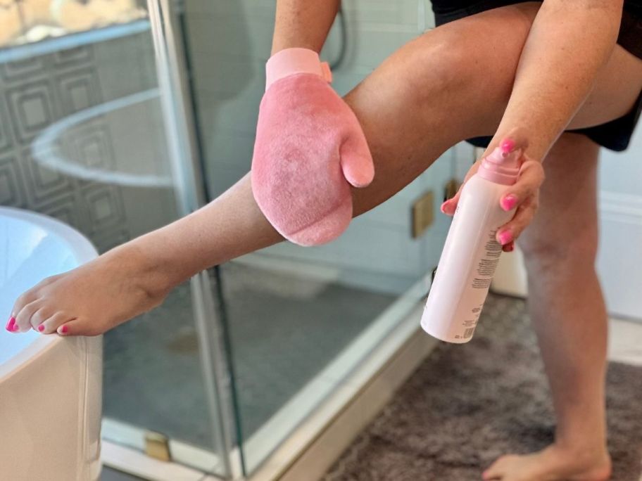 woman applying Tan-Luxe The Future Tanning mist to her leg with a pink mitt