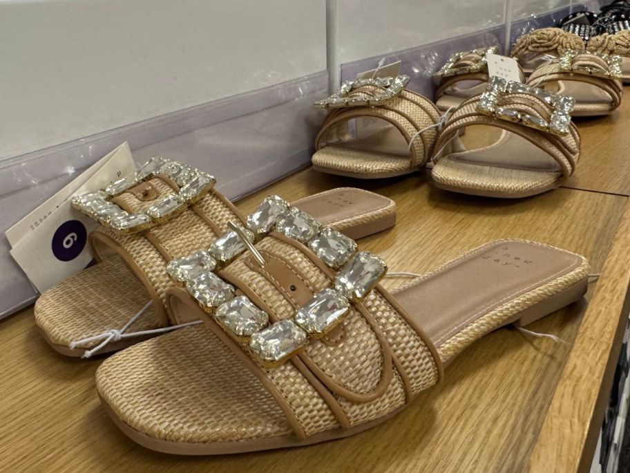 A pair of A New Day Women's Kelsey Rhinestone Buckle Slide Sandals with several of the same shoes lined up in the background
